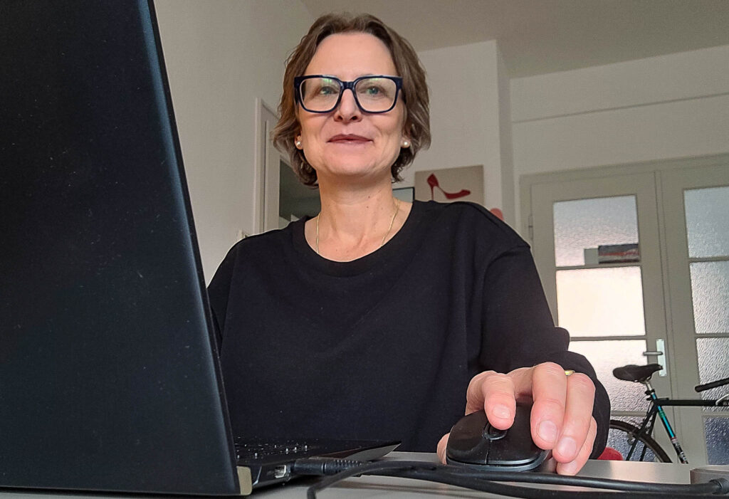 Eine Frau sitzt an Ihrem Computer und schaut in die Kamera